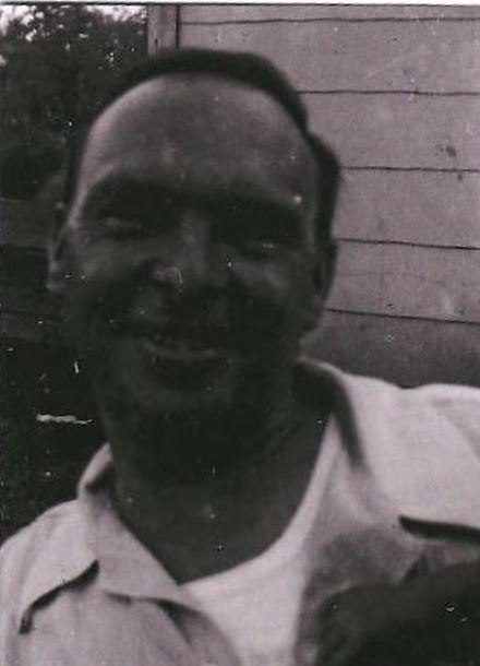 A smiling snapshot of John Edwin Decker in a white shirt beside the depot siding